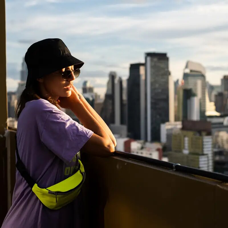 Stylish caucasian woman in trendy panama and waist neon bag on roof in Bangkok